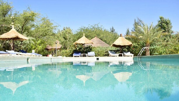Una piscina cristalina con sillas de descanso y sombrillas de paja.