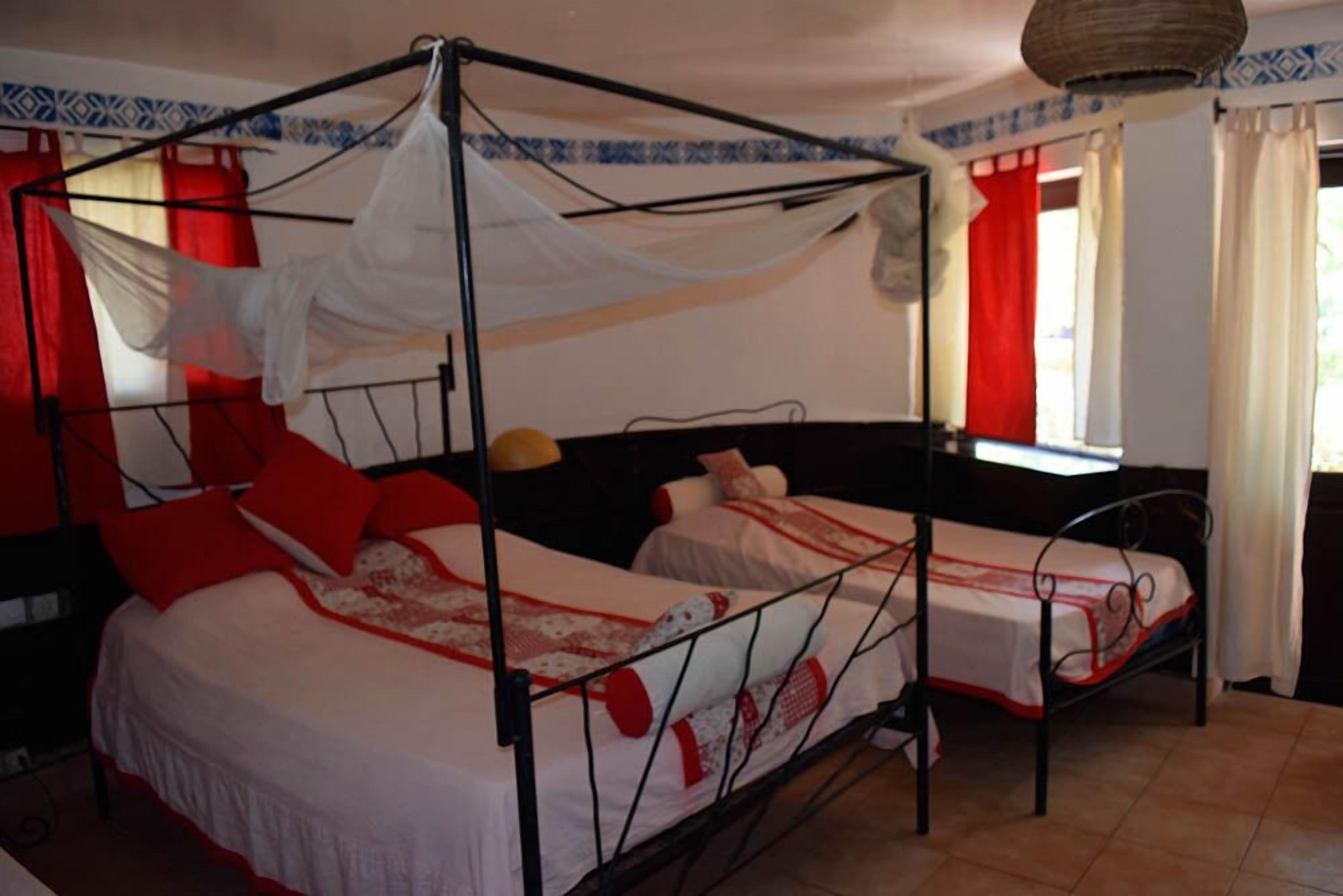 Habitación con dos camas individuales, cada una con dosel. El piso es de baldosas y la pared tiene un diseño estampado.