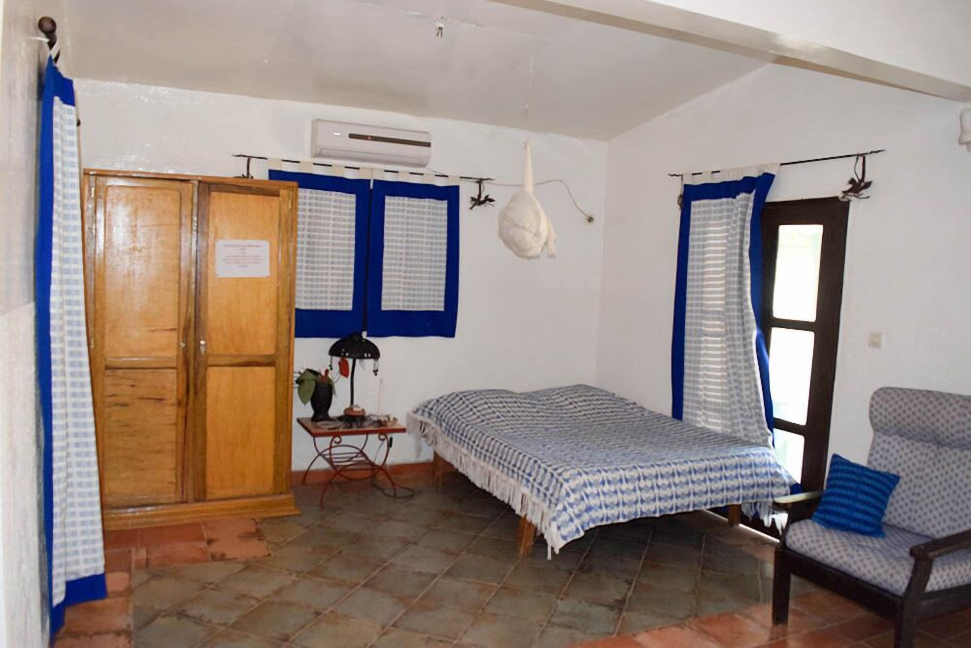 A bedroom with a bed, a chair, a wardrobe, an air conditioner, and a window with curtains.