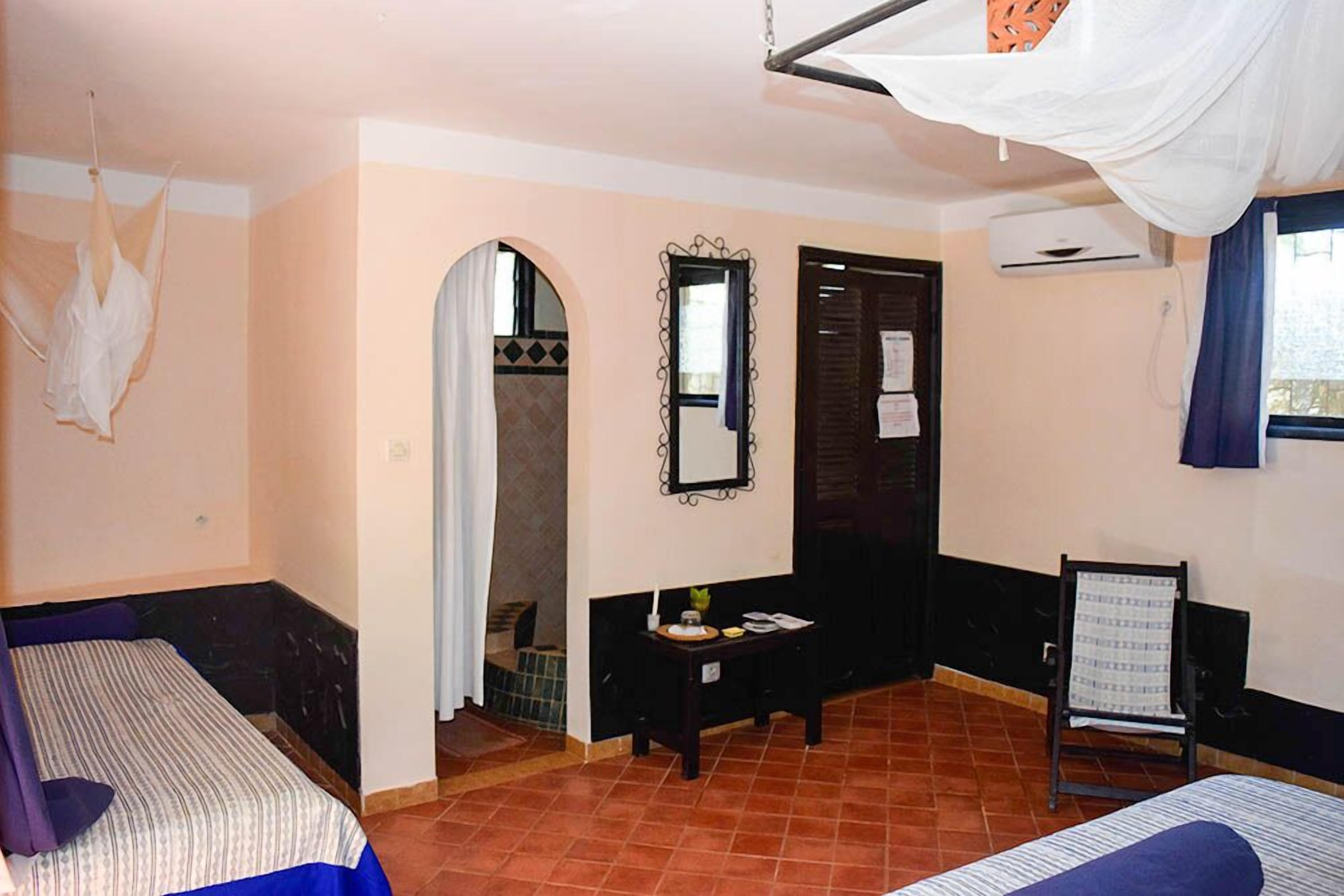 A room with two beds, a small table, a mirror, and a door leading to another room.