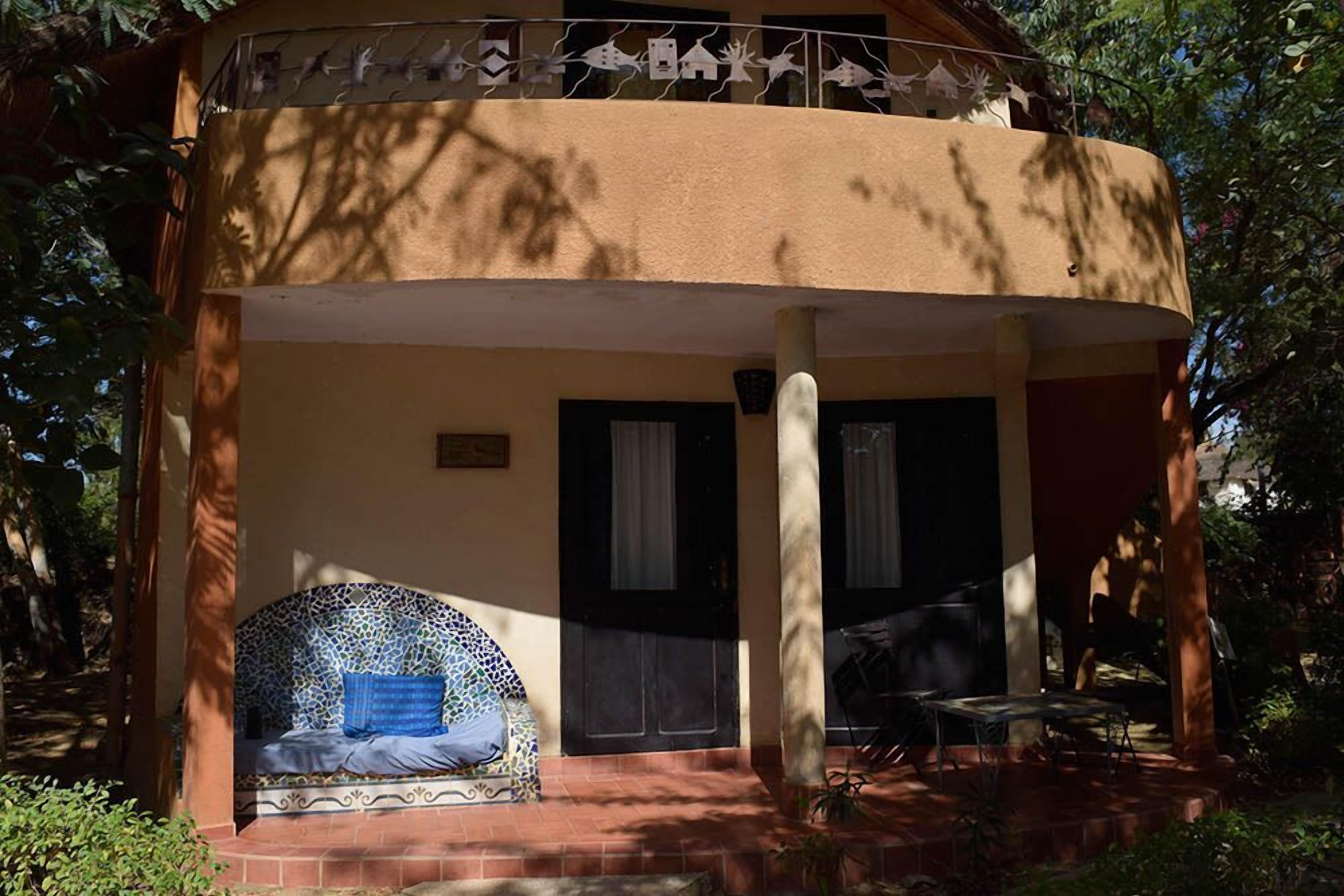 Un bâtiment à deux étages doté d’un balcon, d’un espace de détente couvert avec un canapé à motifs et d’une terrasse avec une table et des chaises.