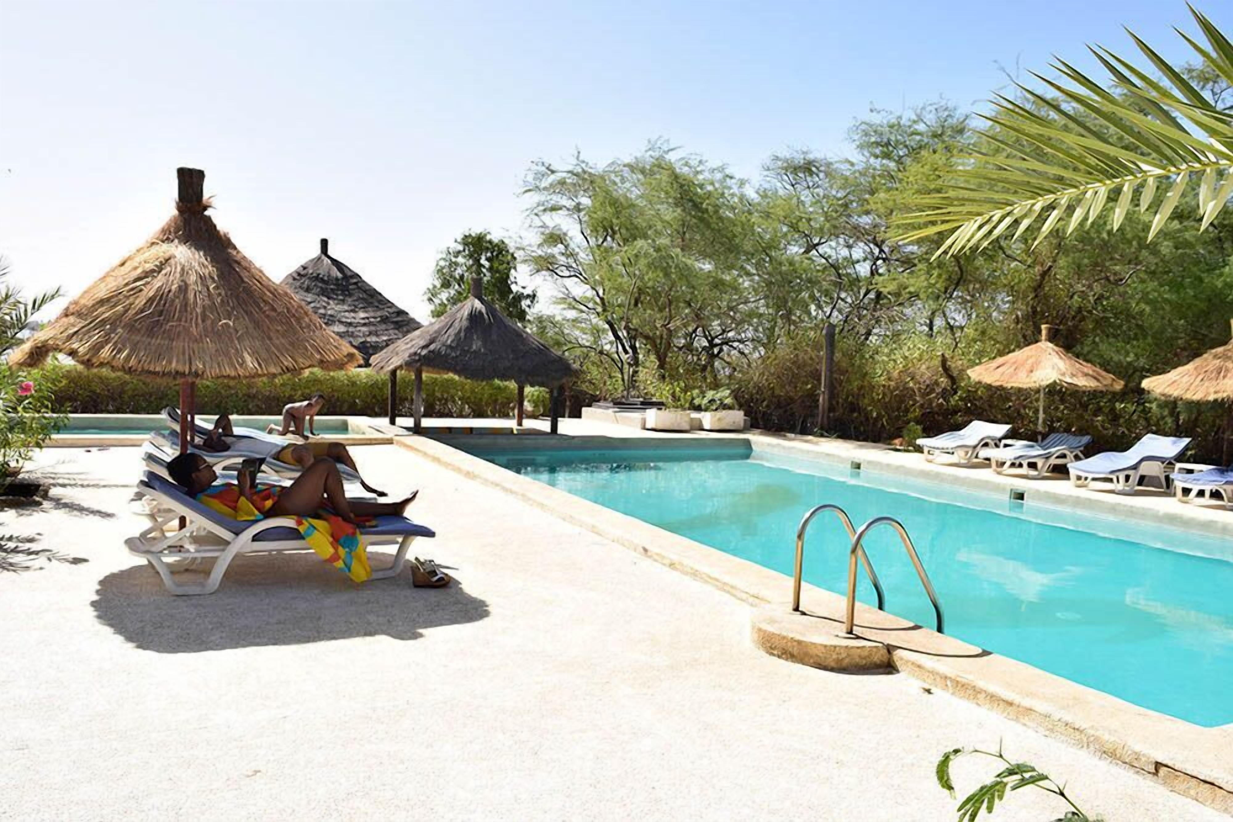 A poolside area with lounge chairs, thatched umbrellas, and a clear blue pool.