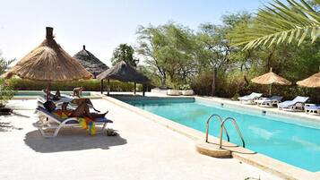 A poolside area with lounge chairs, thatched umbrellas, and a clear blue pool.