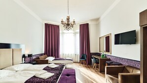Quarto de hotel com cama, duas mesas de cabeceira, escrivaninha, cadeira, televisão e um candelabro.