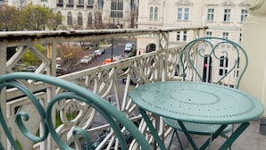 Varanda com duas cadeiras de metal verdes e uma mesa, com vista para um edifício histórico de arquitetura gótica.