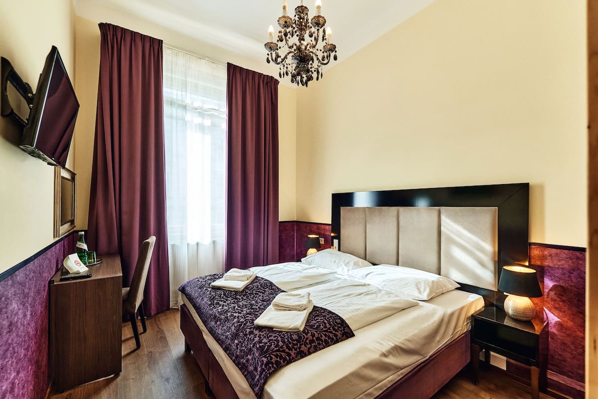 Una habitación de hotel con una cama grande, un escritorio, una silla, un televisor y una araña.
