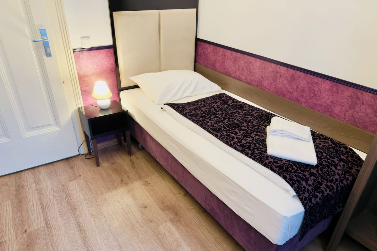 Una cama individual con cabecera, una mesita de noche con lámpara y una puerta.