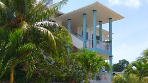 Un immeuble à plusieurs étages doté d’un balcon, entouré d’une végétation luxuriante.