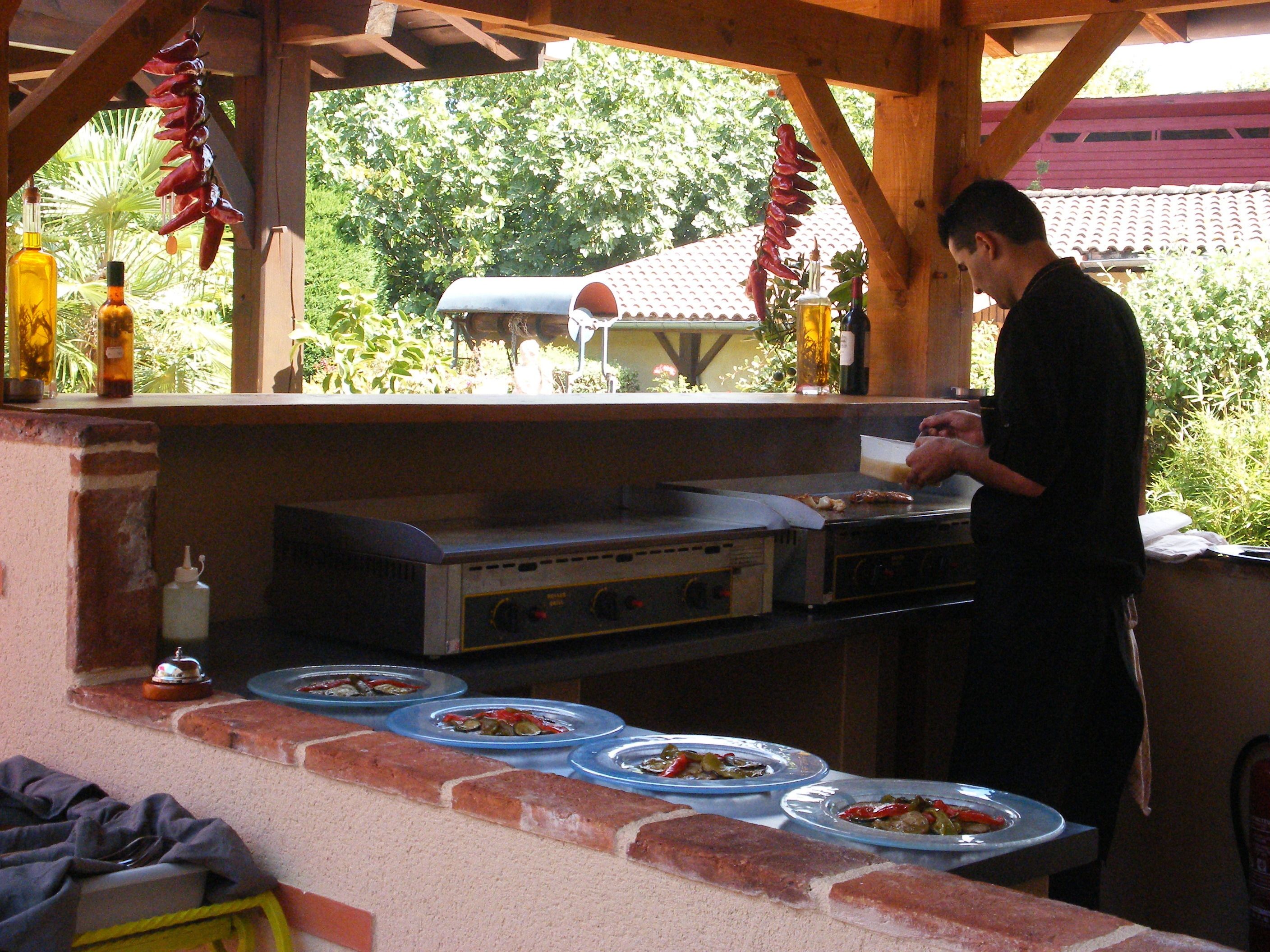 Cocina exterior con una parrilla, utensilios de cocina y platos de comida.