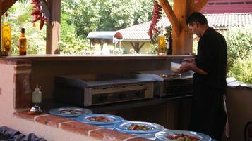 Cocina exterior con una parrilla, utensilios de cocina y platos de comida.