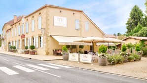 A two-story building with a sign reading "Hotel Restaurant Commerce." There are outdoor tables and chairs under umbrellas, and potted plants are visible. - Logis Hôtel Restaurant Du Commerce (Estang)