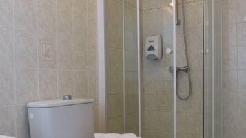 Een badkamer met een toilet, een douchecabine en een zeepdispenser.
