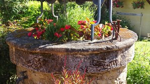 A rustic outdoor water feature with a metal structure, surrounded by lush greenery and flowering plants. - Logis Hôtel Restaurant Du Commerce (Estang)