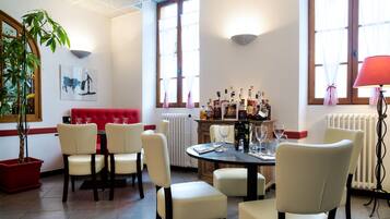 A dining area with a red sofa, white chairs, a round table, and a bar with bottles.
