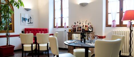 Un área de comedor con un sofá rojo, sillas blancas, una mesa redonda y una barra con botellas.