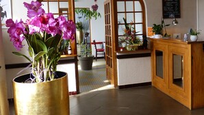 A hotel lobby with a wooden reception desk, a large potted plant, and a mirror reflecting the interior. - Logis Hôtel Restaurant Du Commerce (Estang)