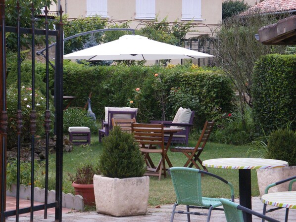 An outdoor patio with a table and chairs, surrounded by potted plants and a hedge.