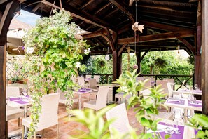 An outdoor patio with wicker chairs and tables, some with purple tablecloths.