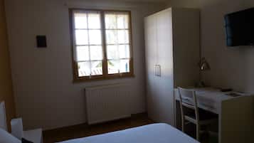 A bedroom with a bed, a desk, a chair, a wardrobe, a radiator, and a window.