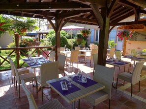 An outdoor patio with tables and chairs, some with umbrellas, surrounded by greenery and plants.