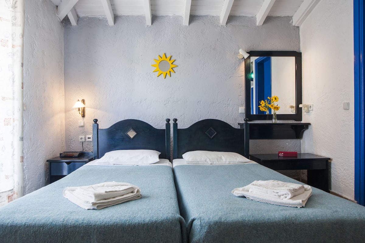 Une chambre avec deux lits, une table de chevet, un miroir et une décoration représentant un soleil au mur.