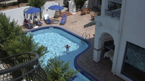 A swimming pool with lounge chairs and umbrellas, surrounded by a white building with a balcony. - Potidea Golden Beach Hotel (Nea Propontida)
