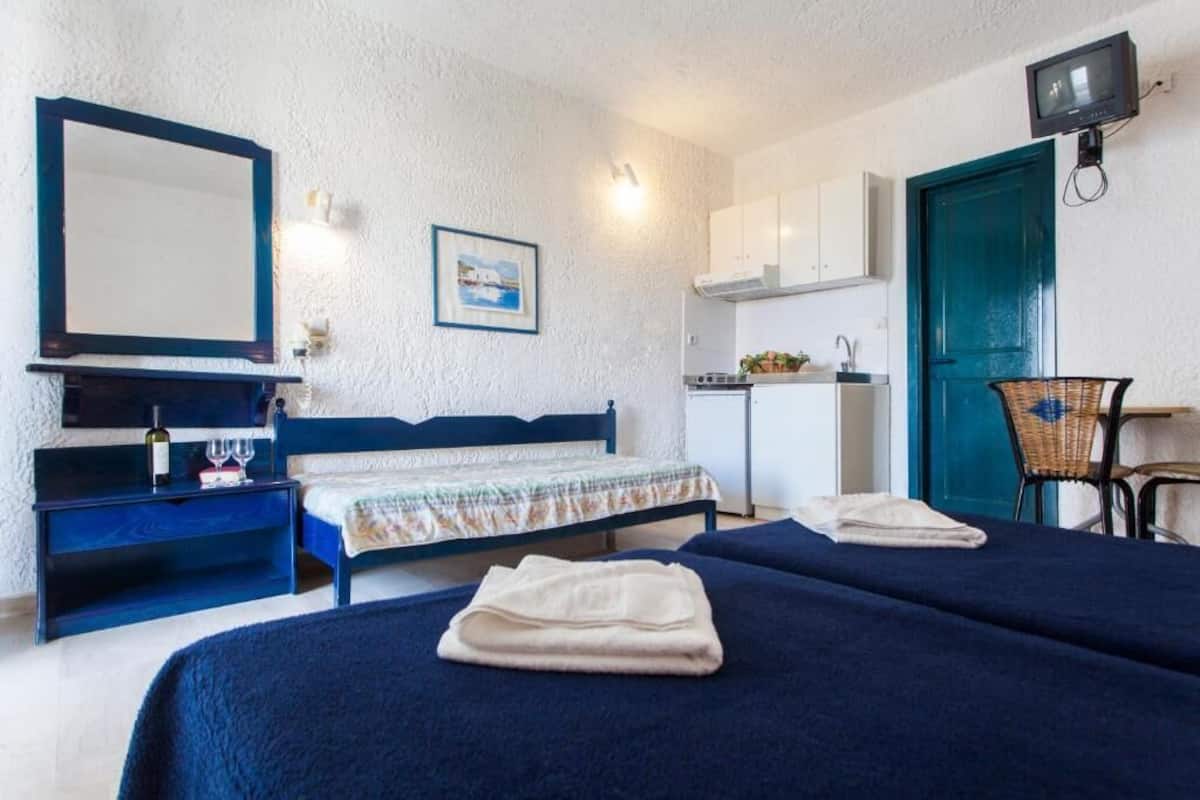 Une chambre avec deux lits, un bureau, une chaise, une télévision et un coin cuisine.