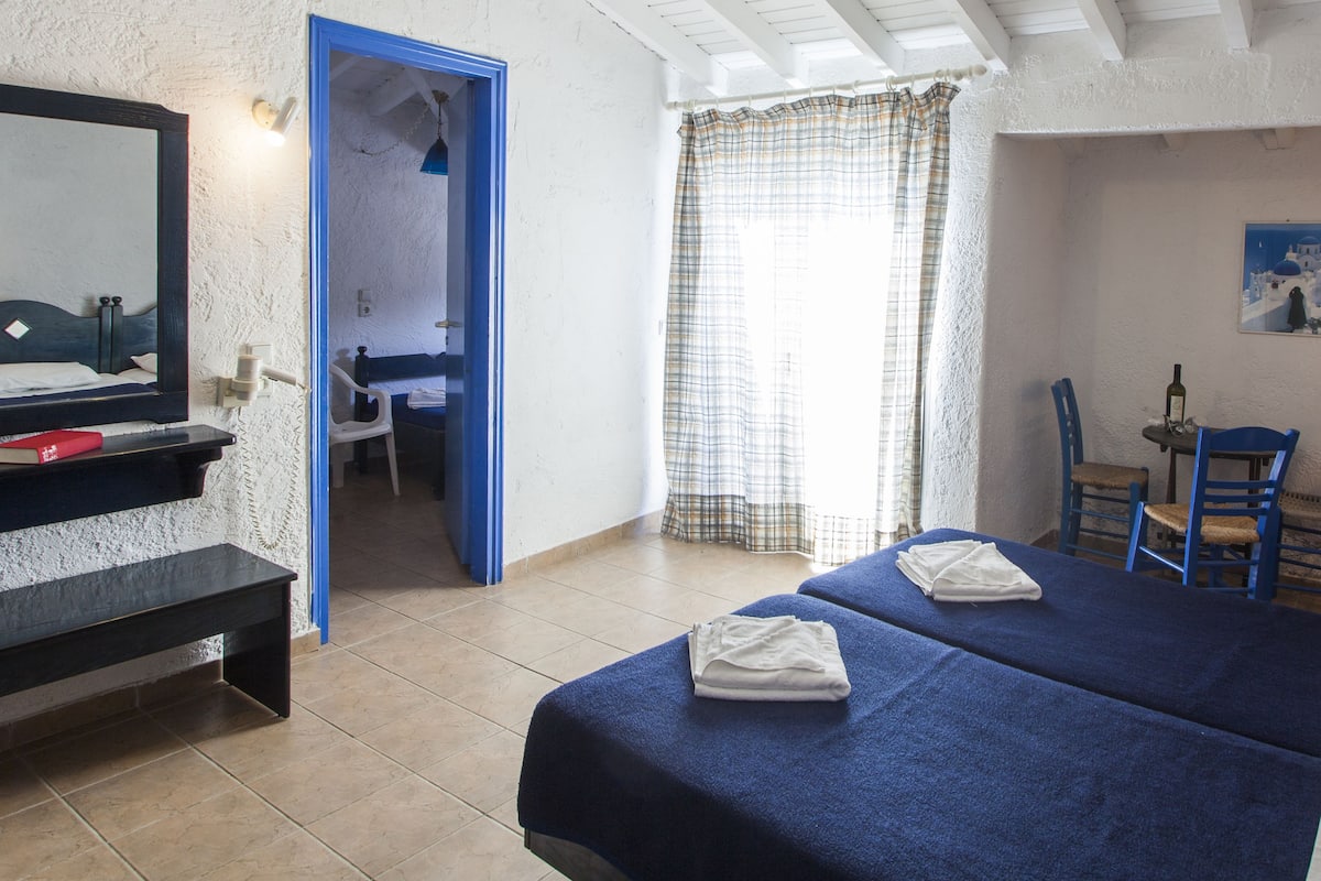 Une chambre d’hôtel avec deux lits, un bureau, une chaise, un miroir et une fenêtre avec des rideaux.