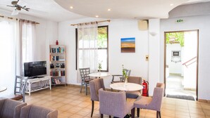 A spacious living area with a television, bookshelves, a dining table, and comfortable seating. - Potidea Golden Beach Hotel (Nea Propontida)