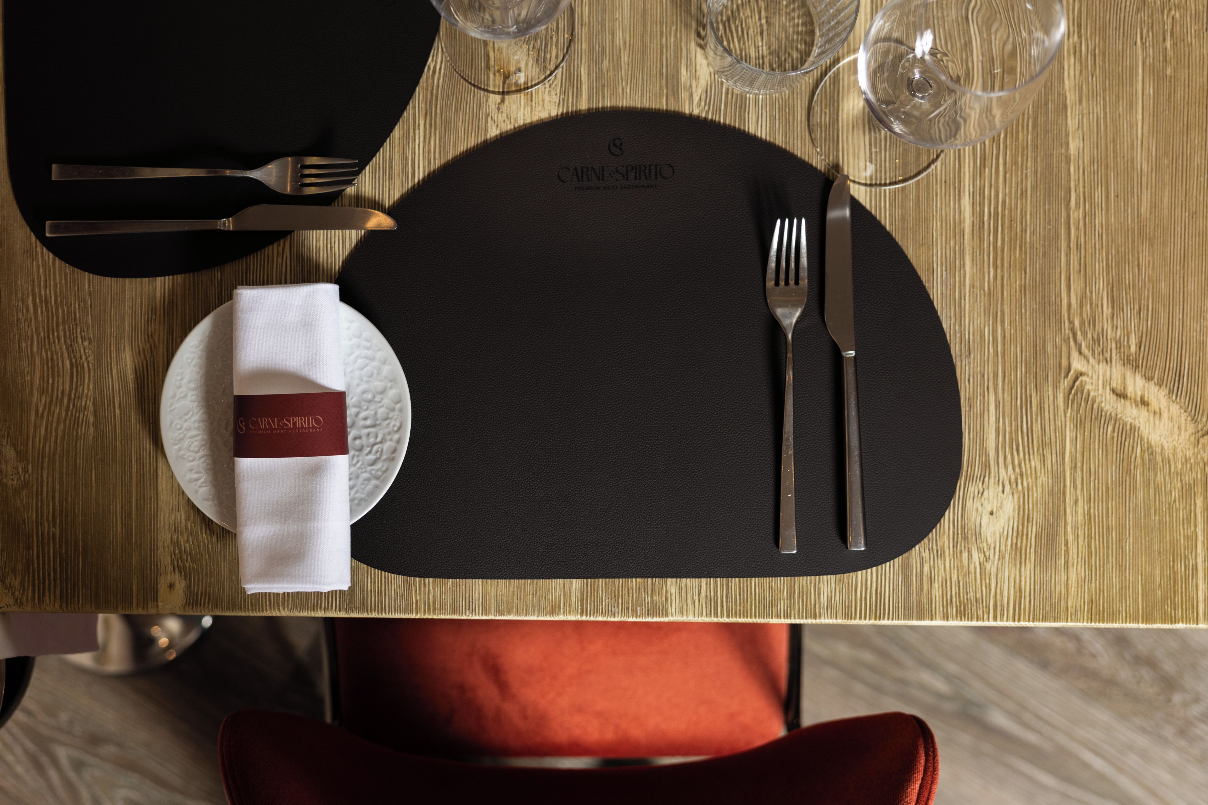 A dining table set with a black placemat, a folded napkin, cutlery, and a glass.