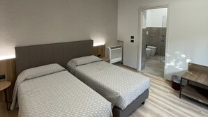 A modern hotel room with two beds, a small table, a bench, and a bathroom visible through a glass door. - Villa Noce - Guest House (Brescia)
