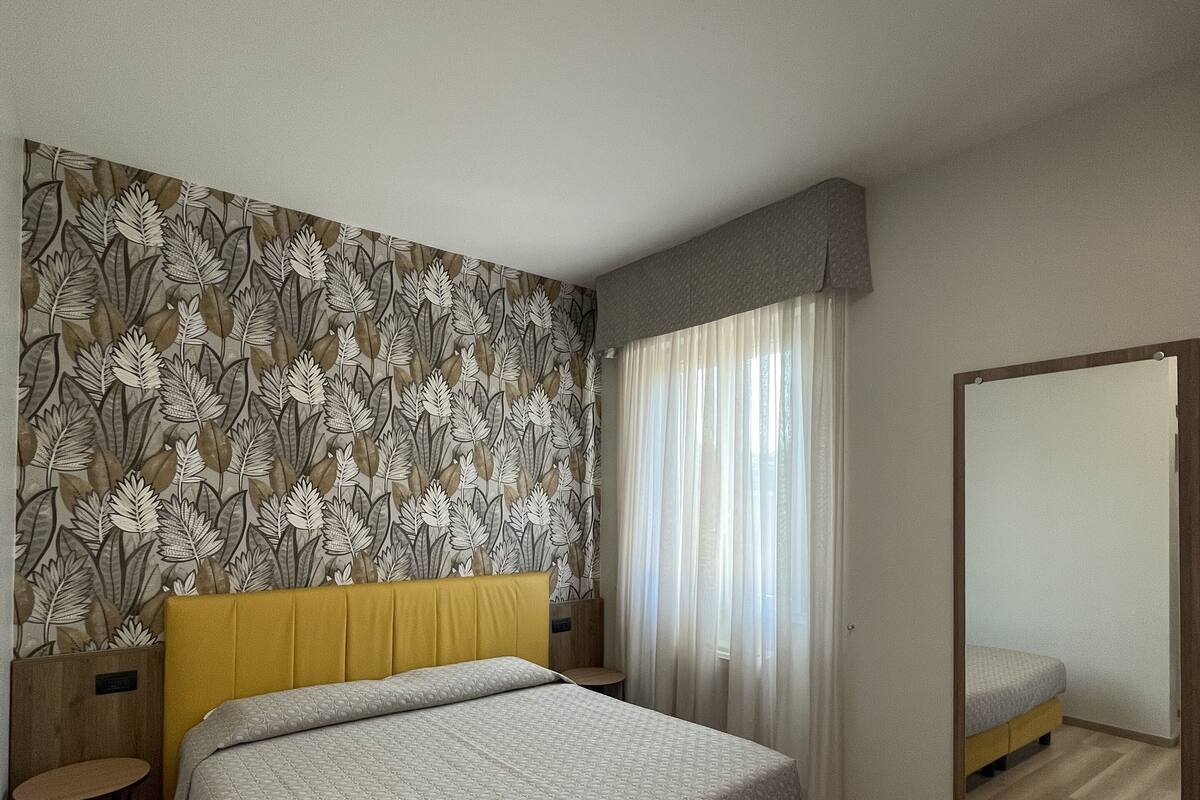 A modern bedroom with a bed, a small table, a mirror, and a patterned wallpaper.