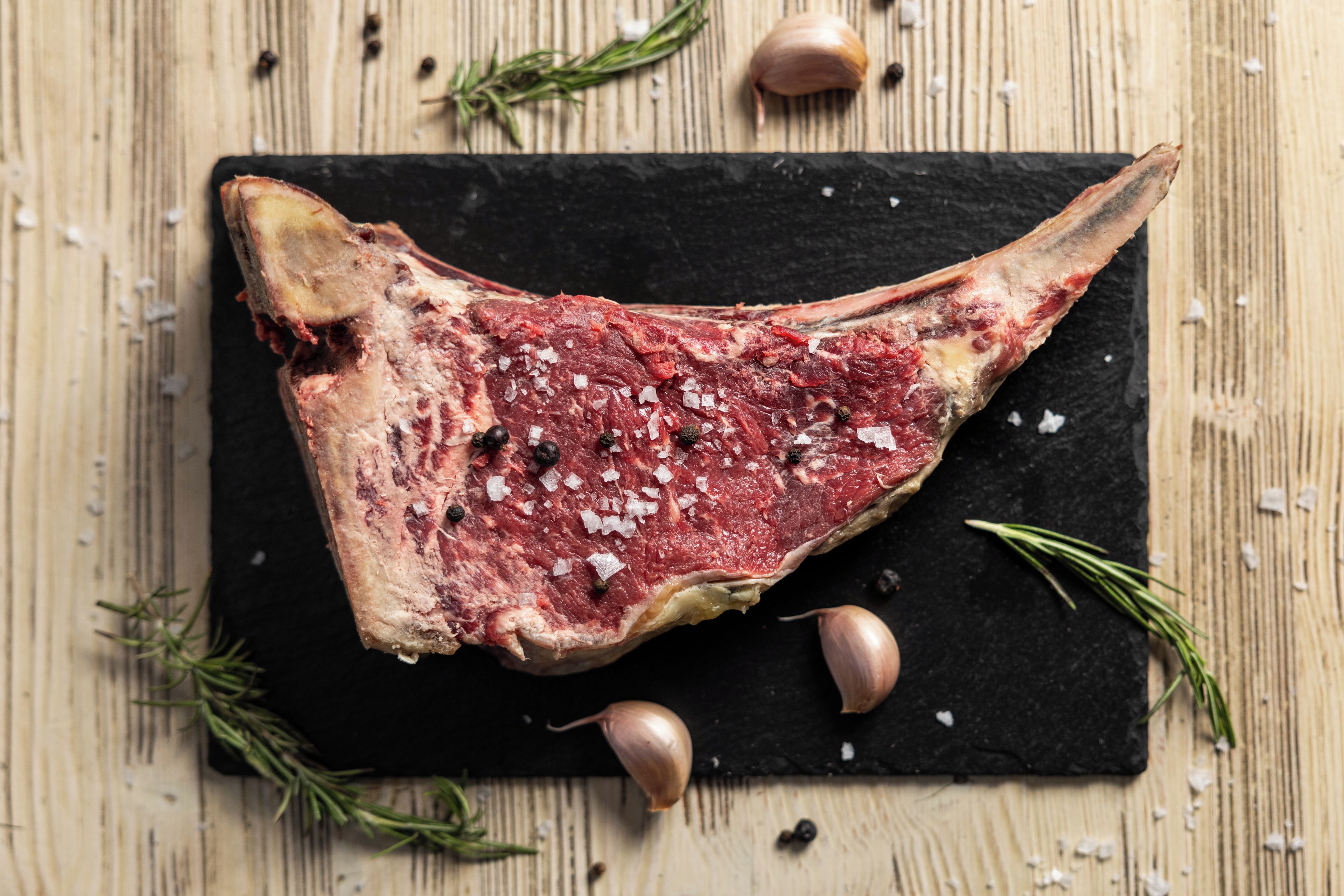 Un bistec sobre una losa negra con ramitas de romero y dientes de ajo alrededor.