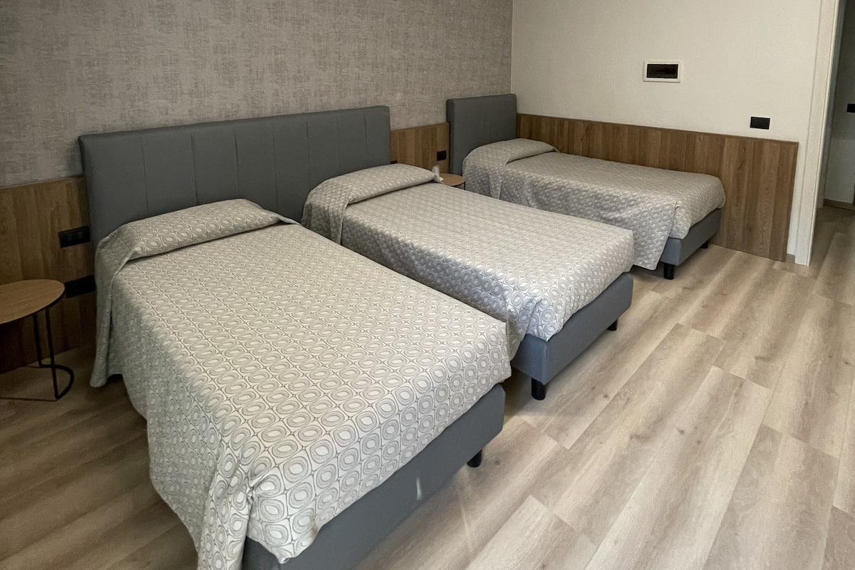 A room with three beds aligned against a wall, a small table, and a door leading to another room.