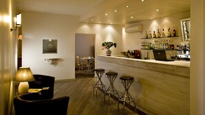A modern bar area with a wooden countertop, bar stools, and a laptop. There is a plant on the wall and a lamp on the left. - Villa Noce - Guest House (Brescia)