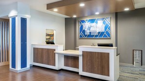 A reception area with a modern design, featuring a reception desk, a digital display, and a blue geometric wall art piece. - Holiday Inn Express & Suites Colorado Springs First & Main by IHG (Colorado Springs)