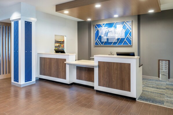 A reception area with a modern design, featuring a reception desk, a digital display, and a blue geometric wall art piece. - Holiday Inn Express & Suites Colorado Springs First & Main by IHG (Colorado Springs)