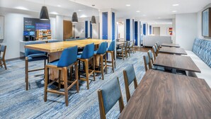 A modern hotel lobby with a long wooden conference table, blue upholstered chairs, and a seating area with blue patterned cushions. - Holiday Inn Express & Suites Colorado Springs First & Main by IHG (Colorado Springs)