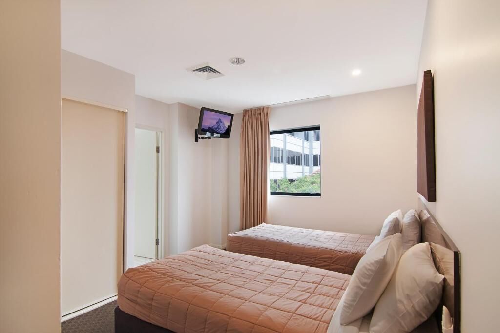 A hotel room with two beds, a TV, a window, and a door.