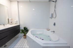 A modern bathroom with a large bathtub, a vanity with dark cabinets, a potted plant, and a handheld showerhead. - Boulevard on Beaumont (Hamilton)