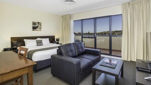A hotel room with a bed, a sofa, a desk, and a large window offering a view of the city. - Boulevard on Beaumont (Hamilton)