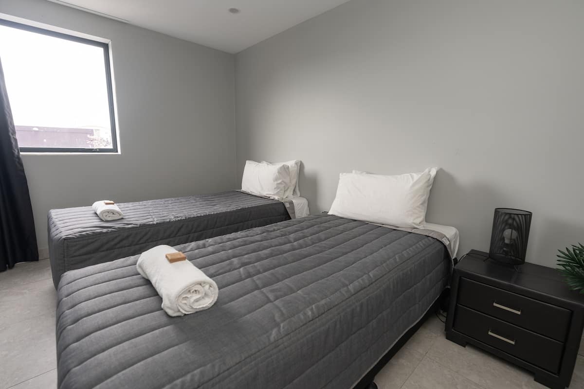 A modern bedroom with two beds, a nightstand, and a window.