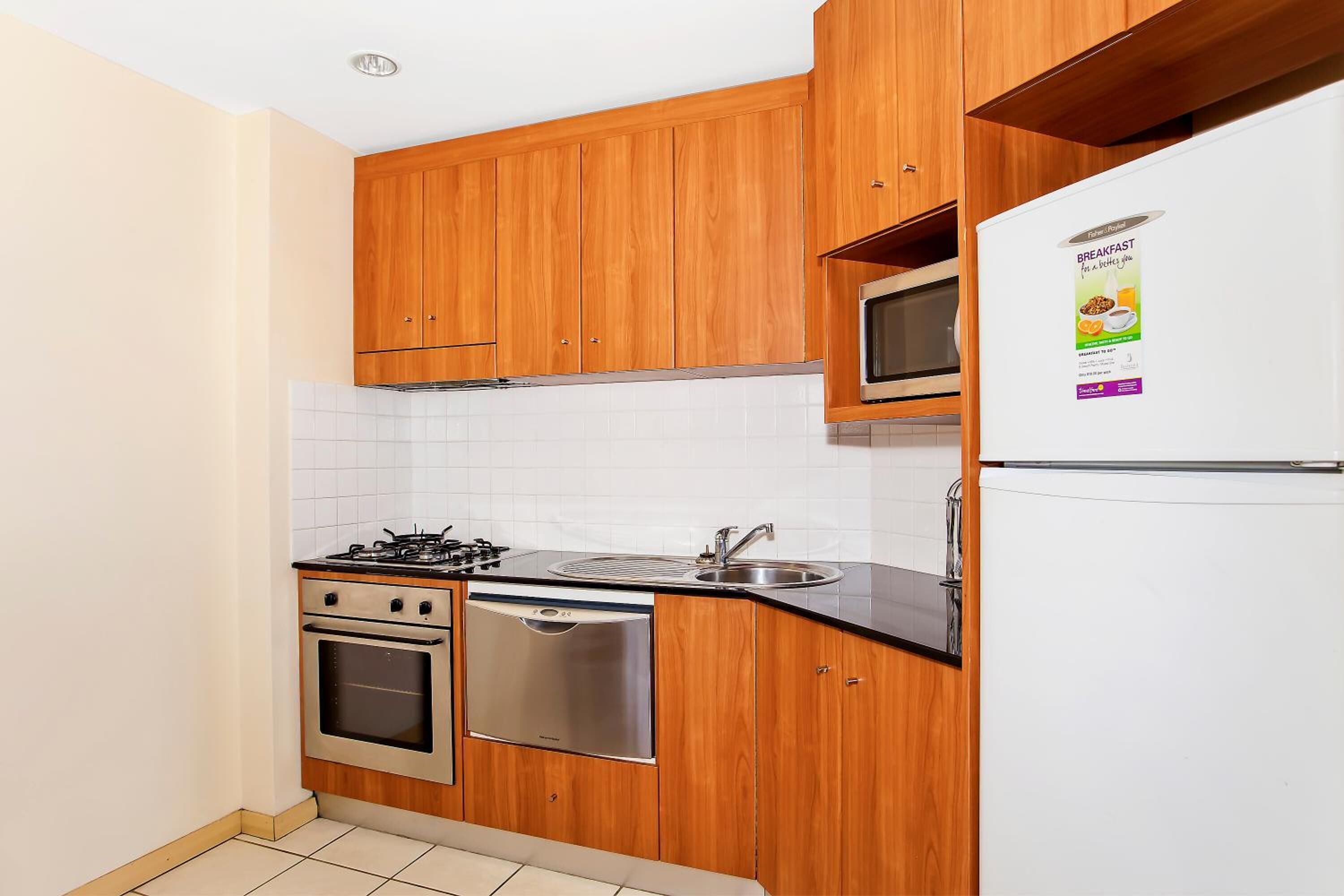 A compact kitchen with wooden cabinets, a gas stove, a dishwasher, a microwave, and a refrigerator.