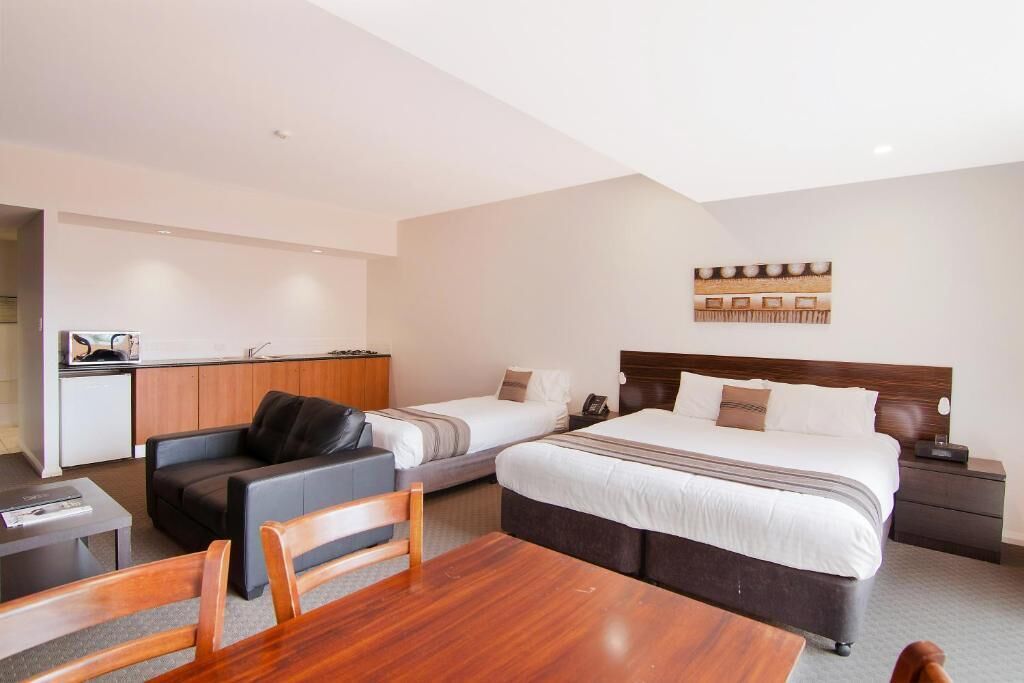 A hotel room with a large bed, a sofa, a dining table, and a kitchenette.