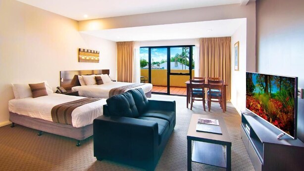 A hotel room with two beds, a sofa, a TV, and a balcony with curtains. - Boulevard on Beaumont (Hamilton)