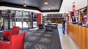 A hotel lobby with a reception desk, red leather chairs, and a patterned carpet. - Boulevard on Beaumont (Hamilton)