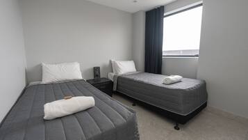A modern hotel room with two beds, a nightstand, a window with curtains, and a view of the outside.
