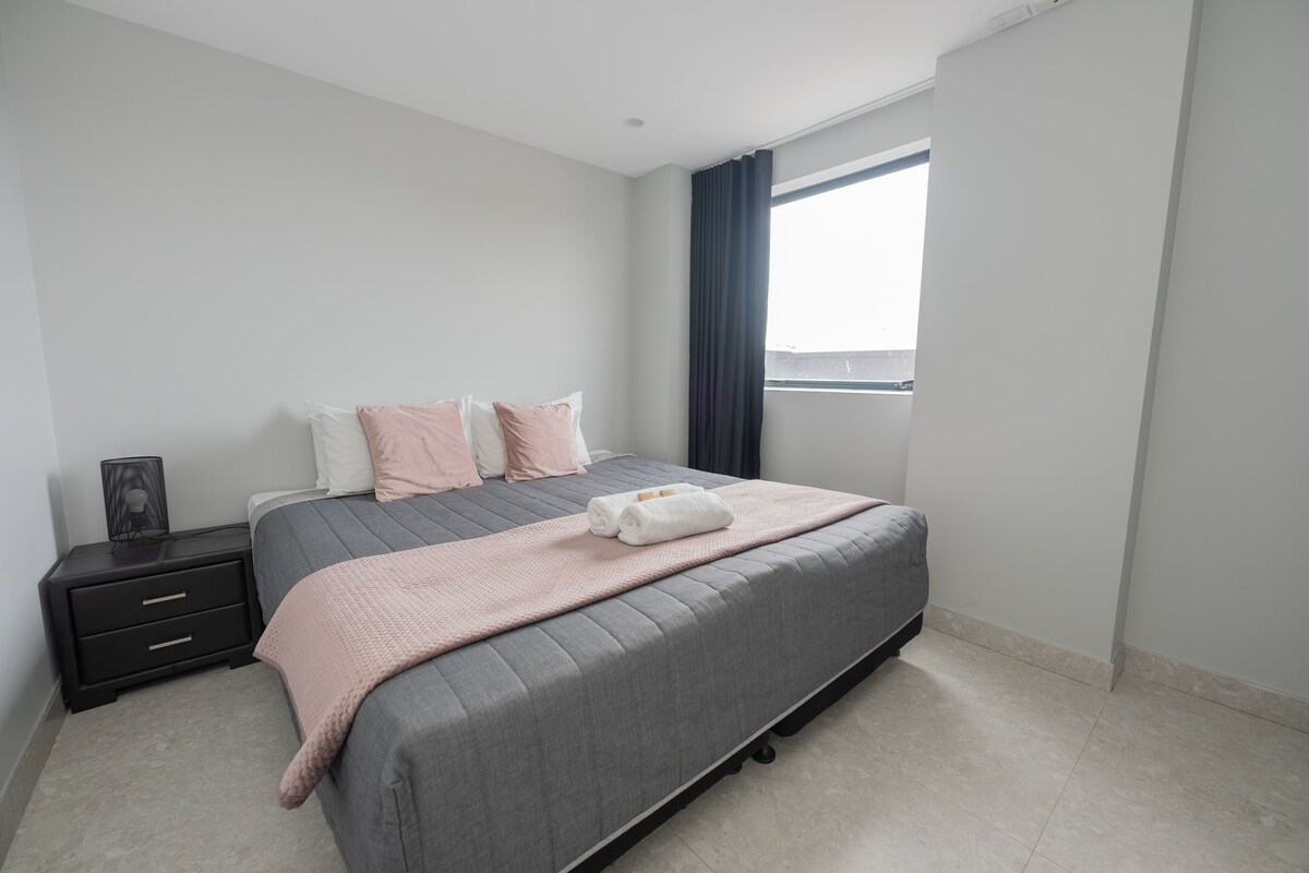 Un dormitorio moderno con cama, mesitas de noche, una ventana y vistas.