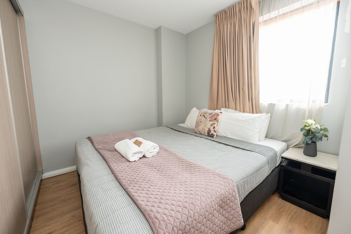 A neatly made bed with a pink quilt, white pillows, and a small plant on the nightstand.