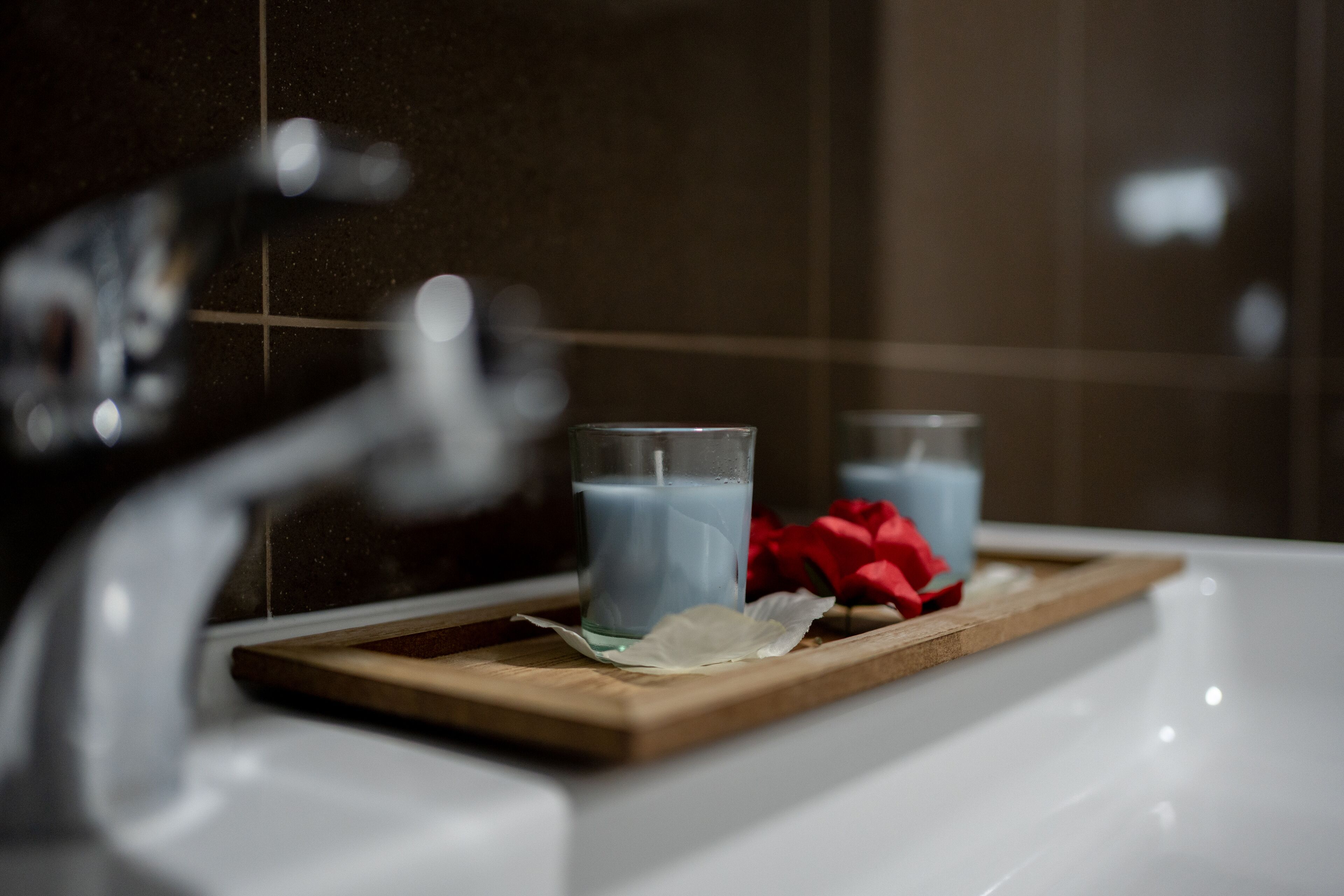 A bathroom with a white sink, two glasses of blue liquid, and a wooden tray with a red rose.